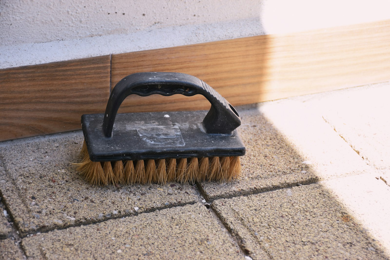 Stiff bristle hand brush resting on pavers between detail scrubbing passes