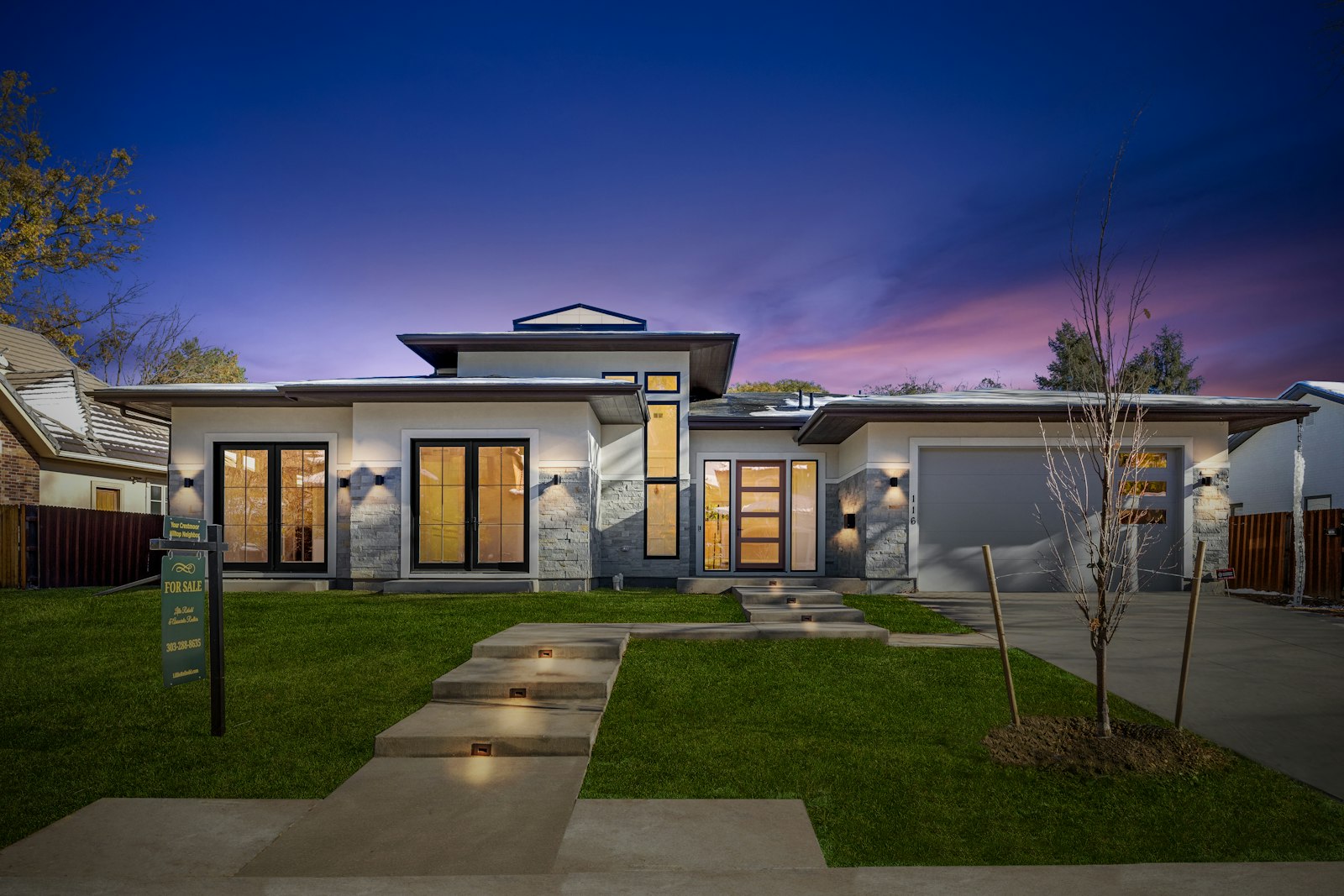 Bright concrete driveway and lit walkway in front of a modern home at dusk