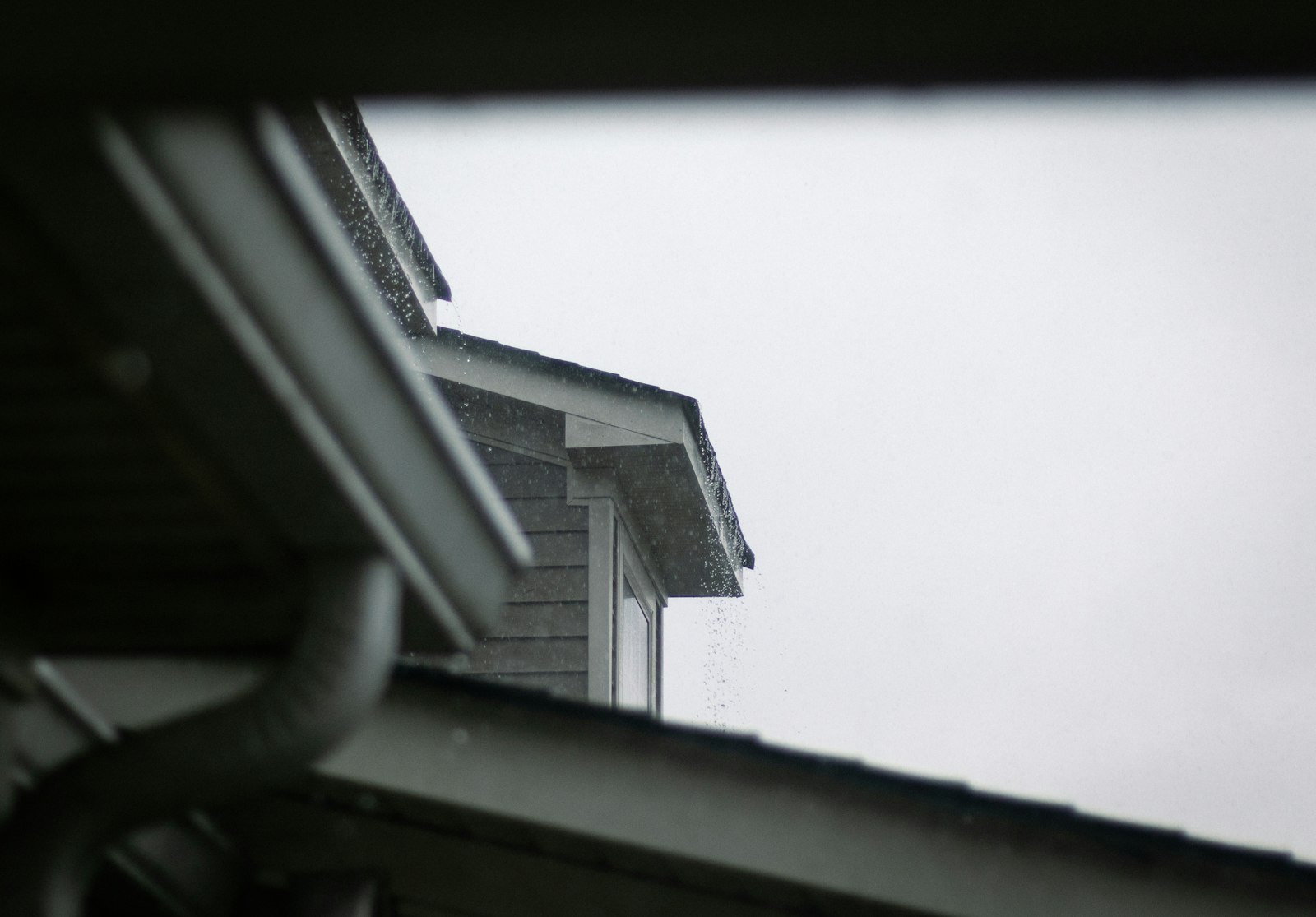 Rain dripping past a roofline and gutter system on an overcast day